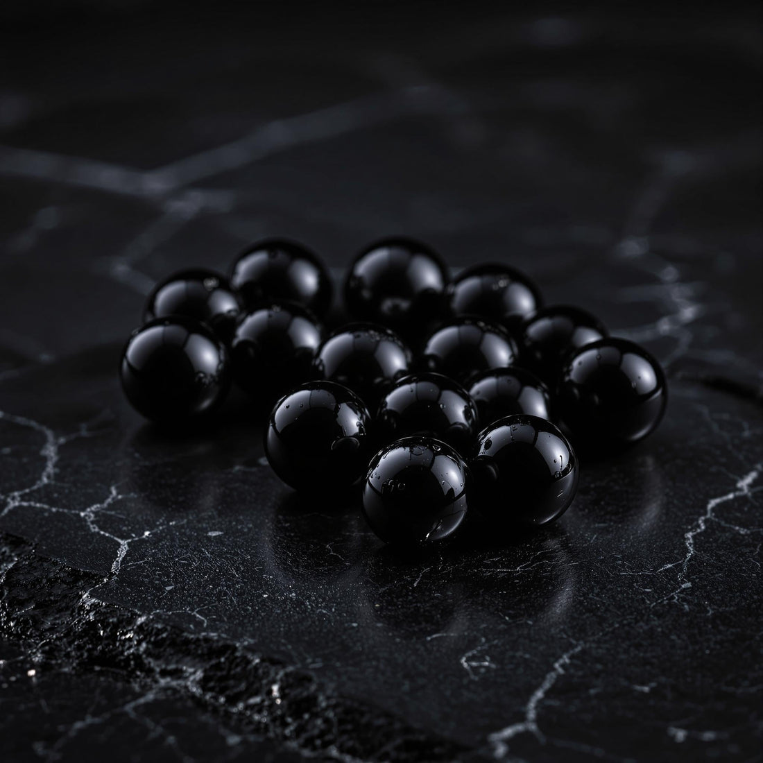 Multiple uniformly-sized black balsamic pearls arranged on a reflective surface with subtle lighting highlighting their spherical shape