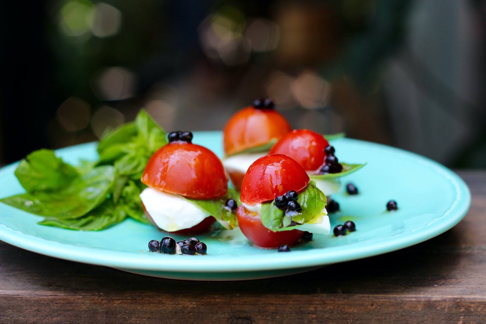 Mini Caprese Salad with Sticky Balsamic Pearls on a blue plate, with mint. on a wooden bench.