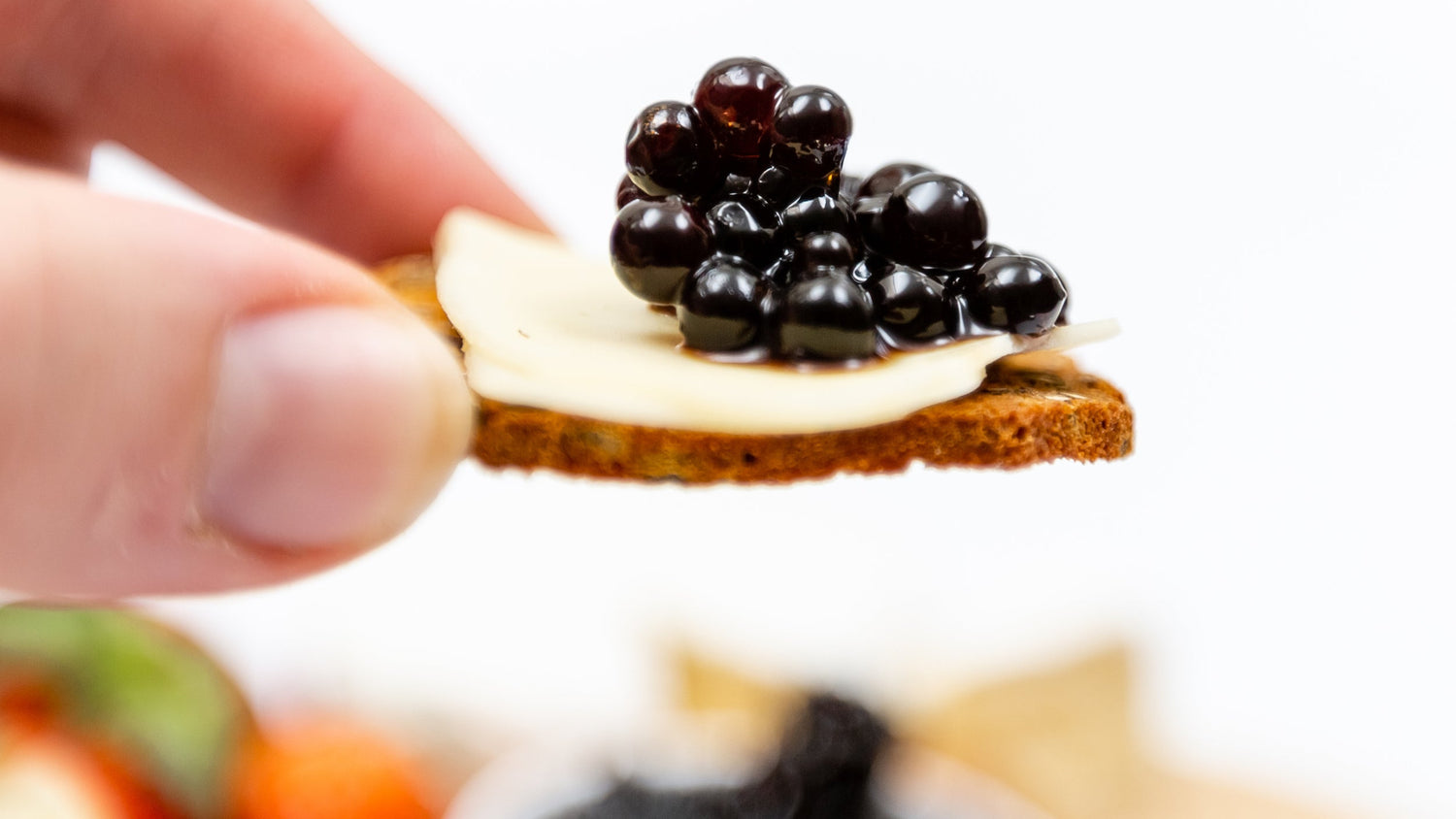 Sticky Balsamic Pearls and cheese cracker being held by thumb and finger with parmesan and pearls on top of a crisp cracker.