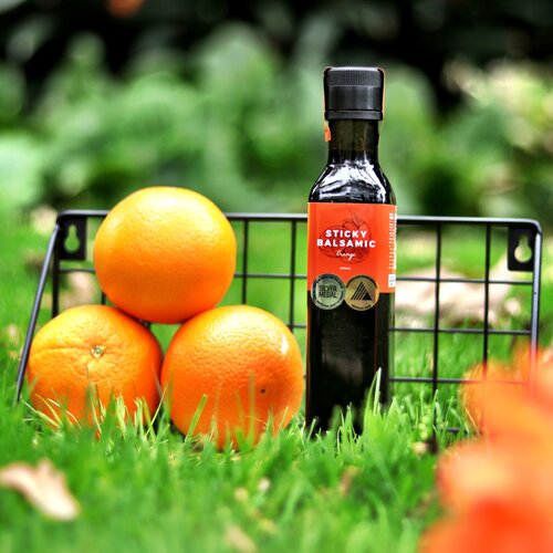 Sticky Balsamic Orange 250ml in a basked with three oranges, with a green fresh natural background