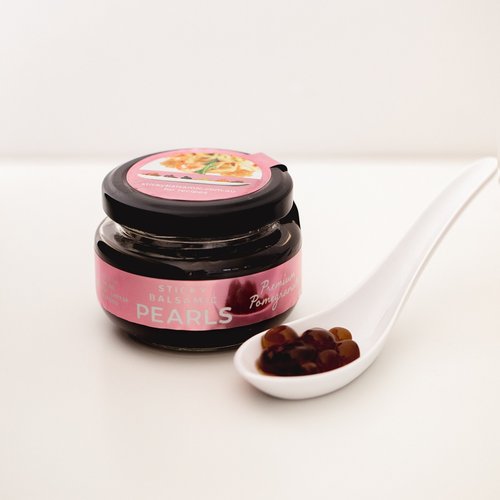 Sticky Balsamic Pearls - Premium Pomegranate jar with a white spoon containing several pearls showing their shape and form. on a white background