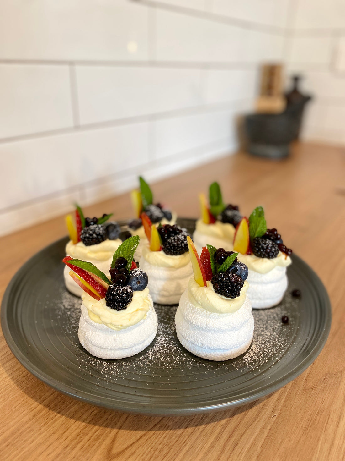 Mini pavlovas topped with whipped cream, fresh blackberries, blueberries, apple slices, mint leaves and Sticky Balsamic Original Pearls on a grey plate