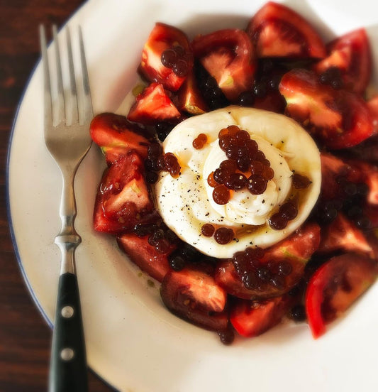 tomatoes, burrata, sticky balsamic pearls on a white plate and a spoon.