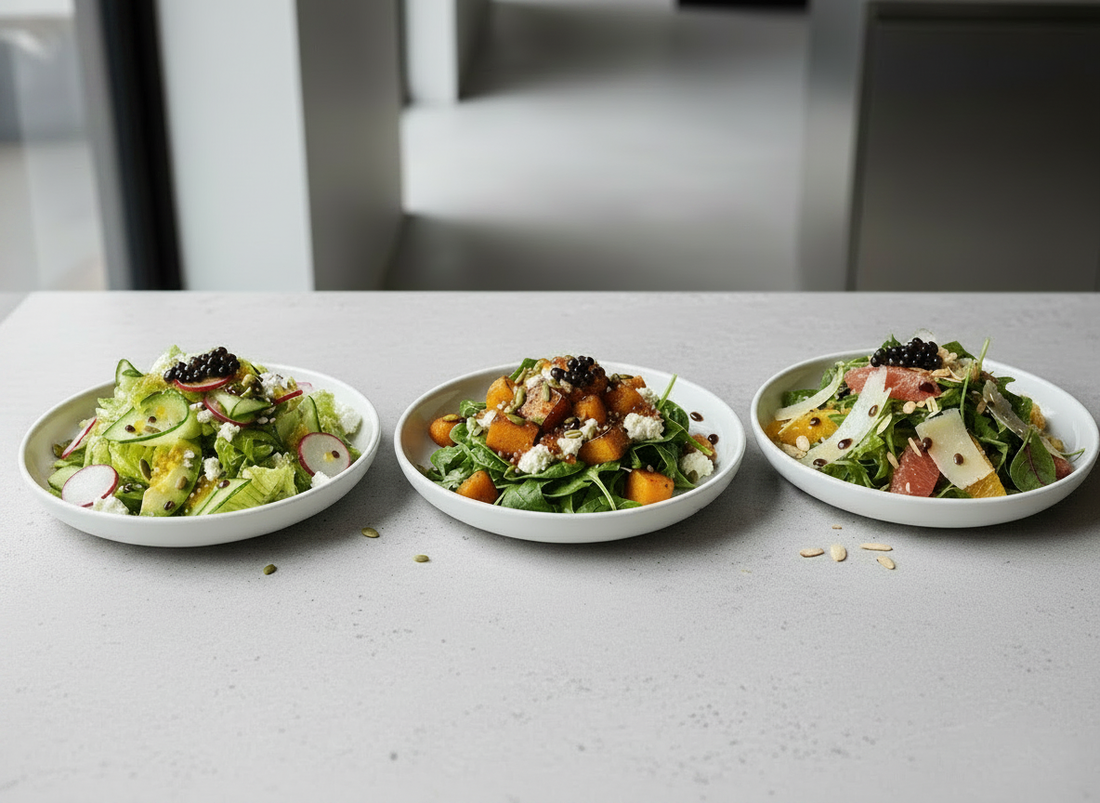 Three plated restaurant-style salads on a light stone bench, finished with balsamic dressing and dark balsamic pearls.