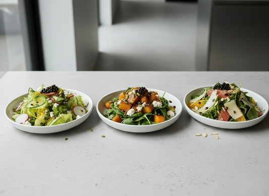 Three plated restaurant-style salads on a light stone bench, finished with balsamic dressing and dark balsamic pearls.