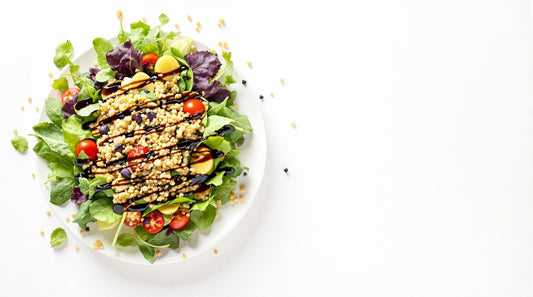 Fresh leaf and grain salad drizzled with simply balsamic dressing on a white background, featuring quinoa and mixed greens in a minimalist presentation