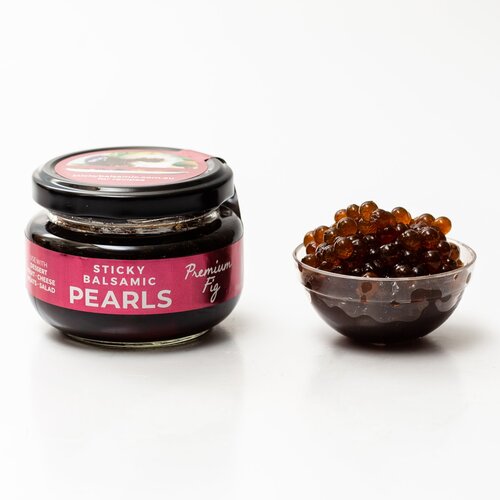 Sticky Balsamic Premium Fig Pearls in a jar and some next to the jar in a plastic container with a white background.