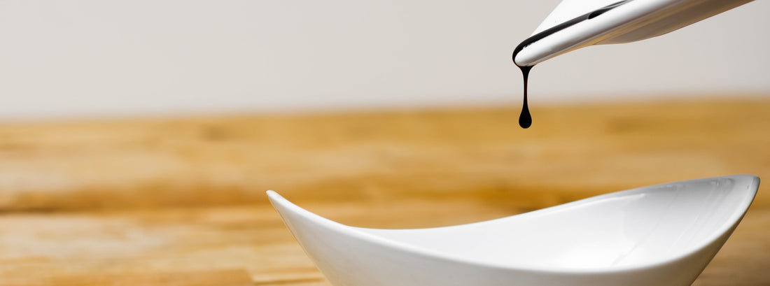 A single drop of balsamic transferring from a white spoon to a white container on a wooden board. Can balsamic vinegar go bad.