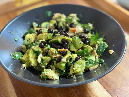Fresh tuna salad with diced avocado, cucumber, parsley and Sticky Balsamic Lemon Pearls served in black bowl on wooden table