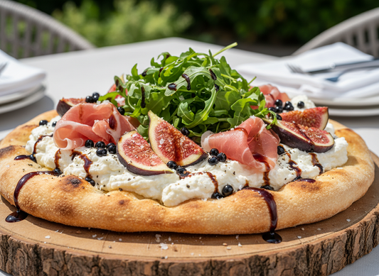 Flatbread on a wooden board topped with whipped ricotta, folded prosciutto slices, fresh fig slices, rocket (arugula), glossy dark Sticky Balsamic Fig Pearls, and a generous, natural-looking drizzle of dark balsamic vinegar. 