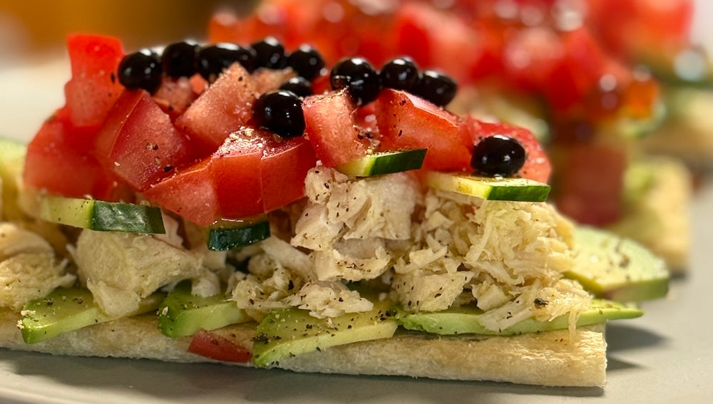 Gourmet cracker topped with sliced avocado, flaked tuna, cucumber, tomato, and Sticky Balsamic Original Pearls on a white plate