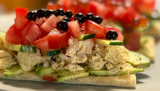 Gourmet cracker topped with sliced avocado, flaked tuna, cucumber, tomato, and Sticky Balsamic Original Pearls on a white plate