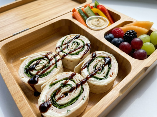 overhead lunchbox with pinwheel wraps drizzled with Sticky Balsamic, alongside veggie sticks and fruit