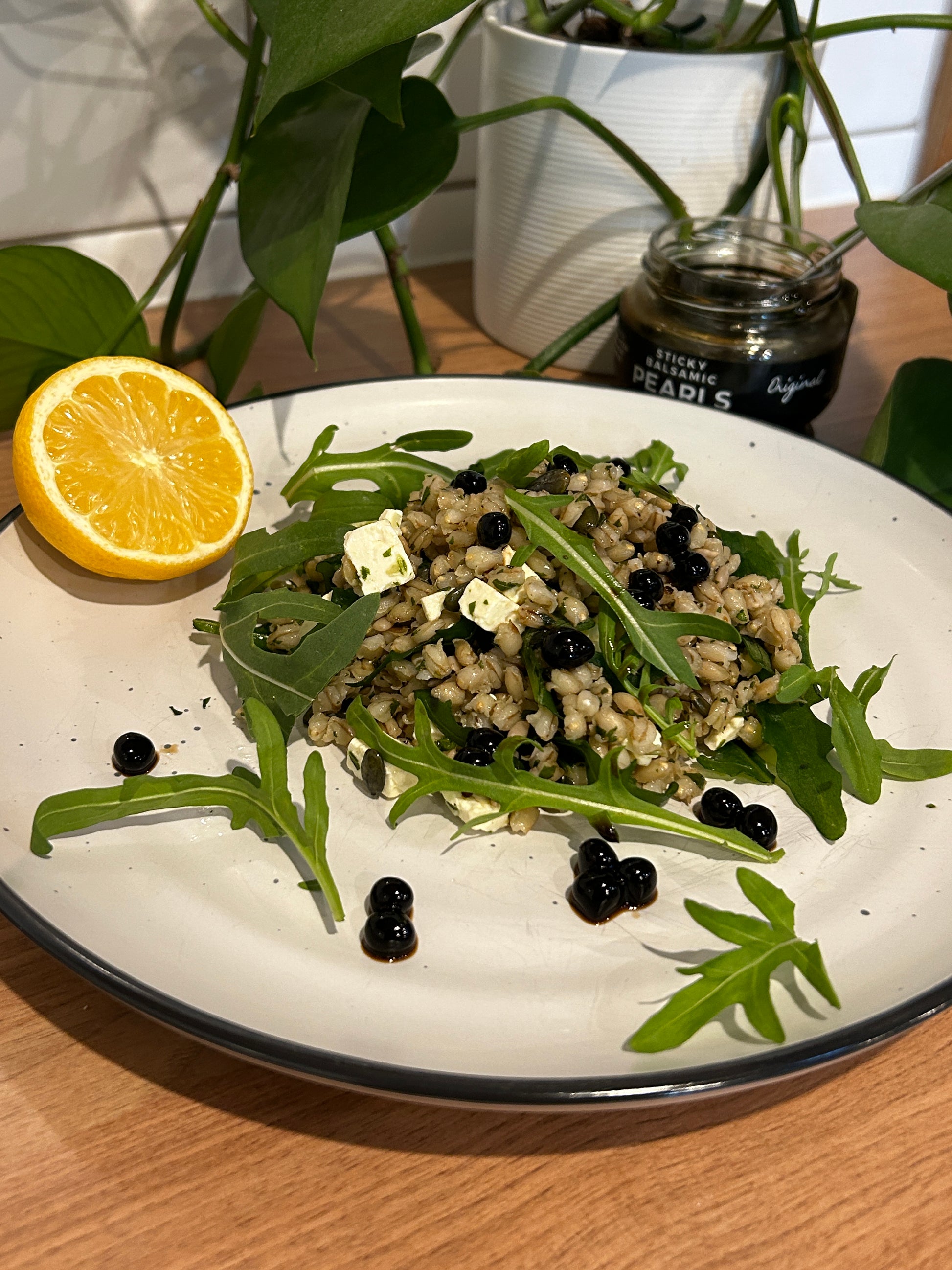 Sticky Balsamic Pearls Original on a pearl barley salad  and rocket, feta with orange  with an open jar of pearls and a green plant behind it.