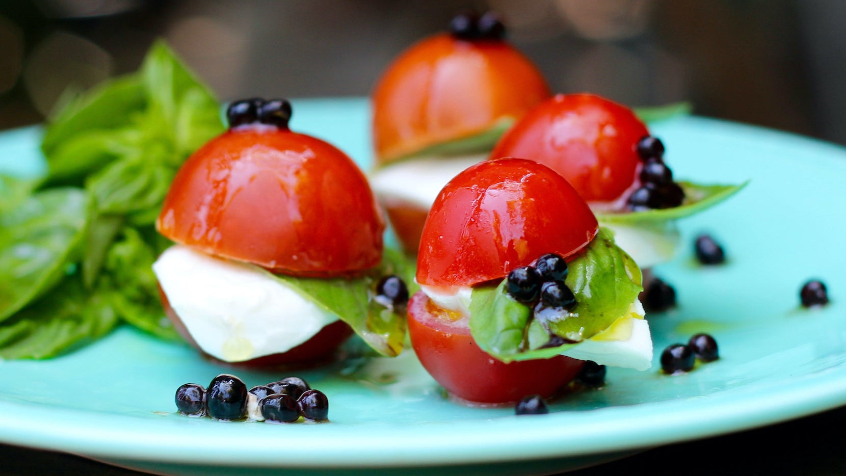 Stuffed cherry tomatoes with white cheese, basil leaves, and balsamic pearls