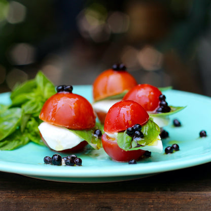 Sticky Balsamic Original Pearls Mini Caprese Salad with roma tomatoes, buffalo mozzarella, basil and Sticky Balsamic Pearls on a blue plate