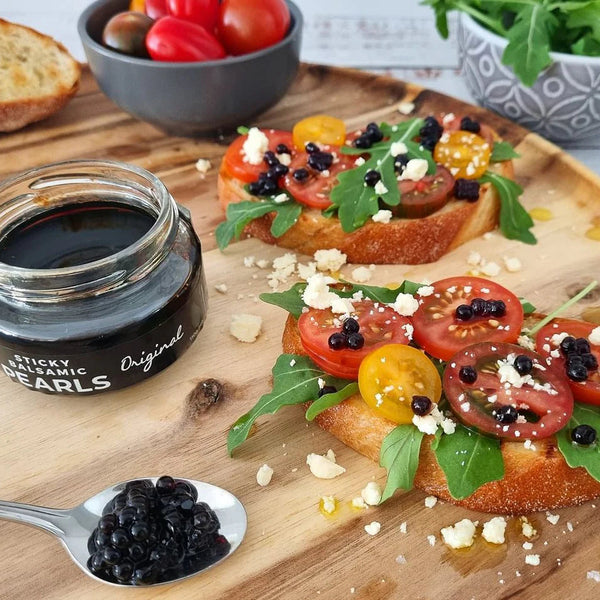 Jar of Sticky balsamic Pearls product on a wooden board garnishing bruschetta.