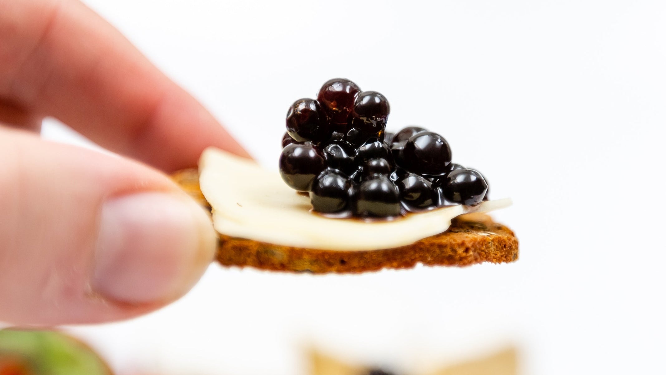 Sticky Balsamic Pearls on top of a slice of gourmet cheese, on a cracker with an artistically blurred background indicating a cheese and charcuterie platter.