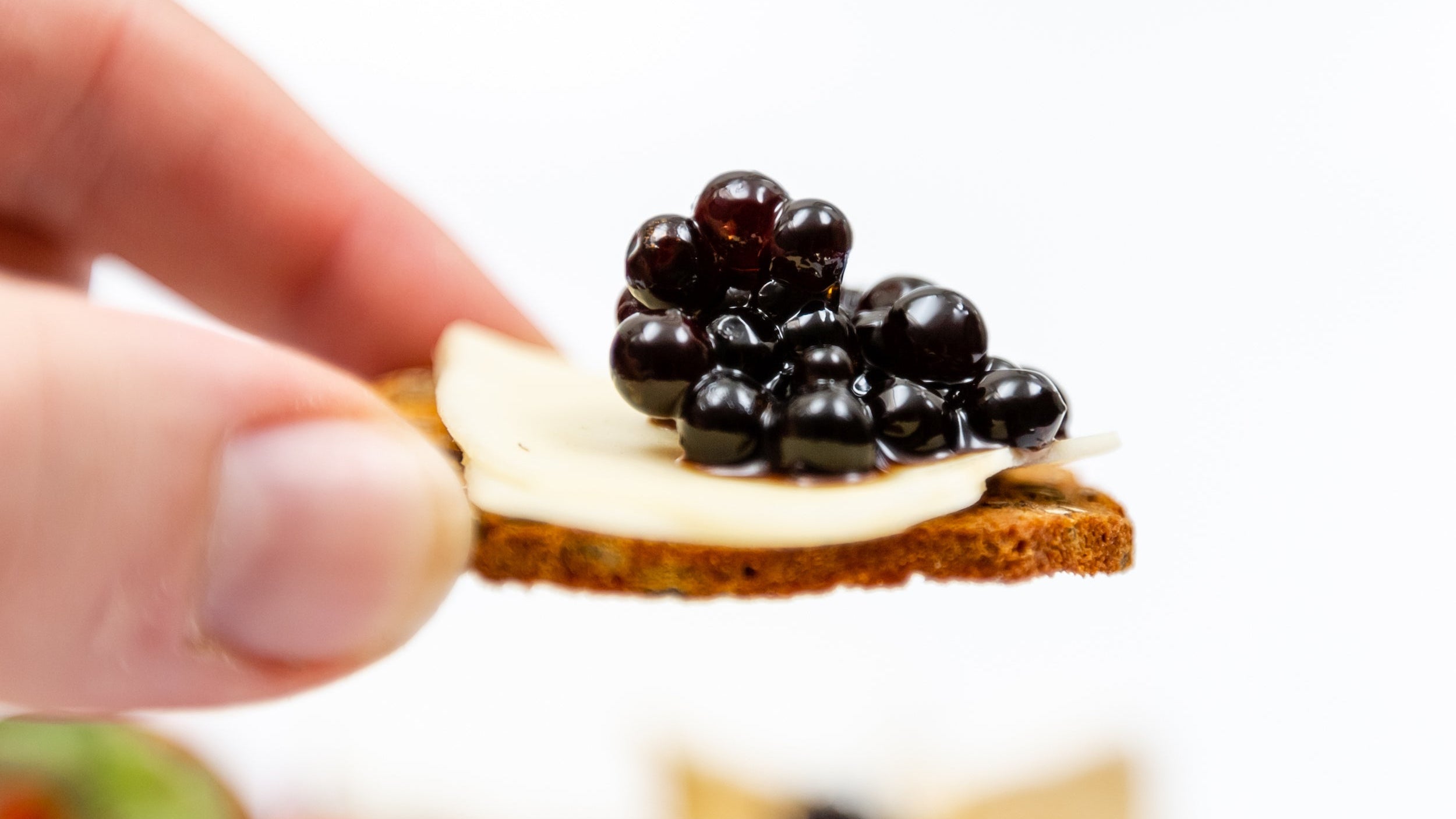 Sticky Balsamic Pearls on top of a slice of gourmet cheese, on a cracker with an artistically blurred background indicating a cheese and charcuterie platter.